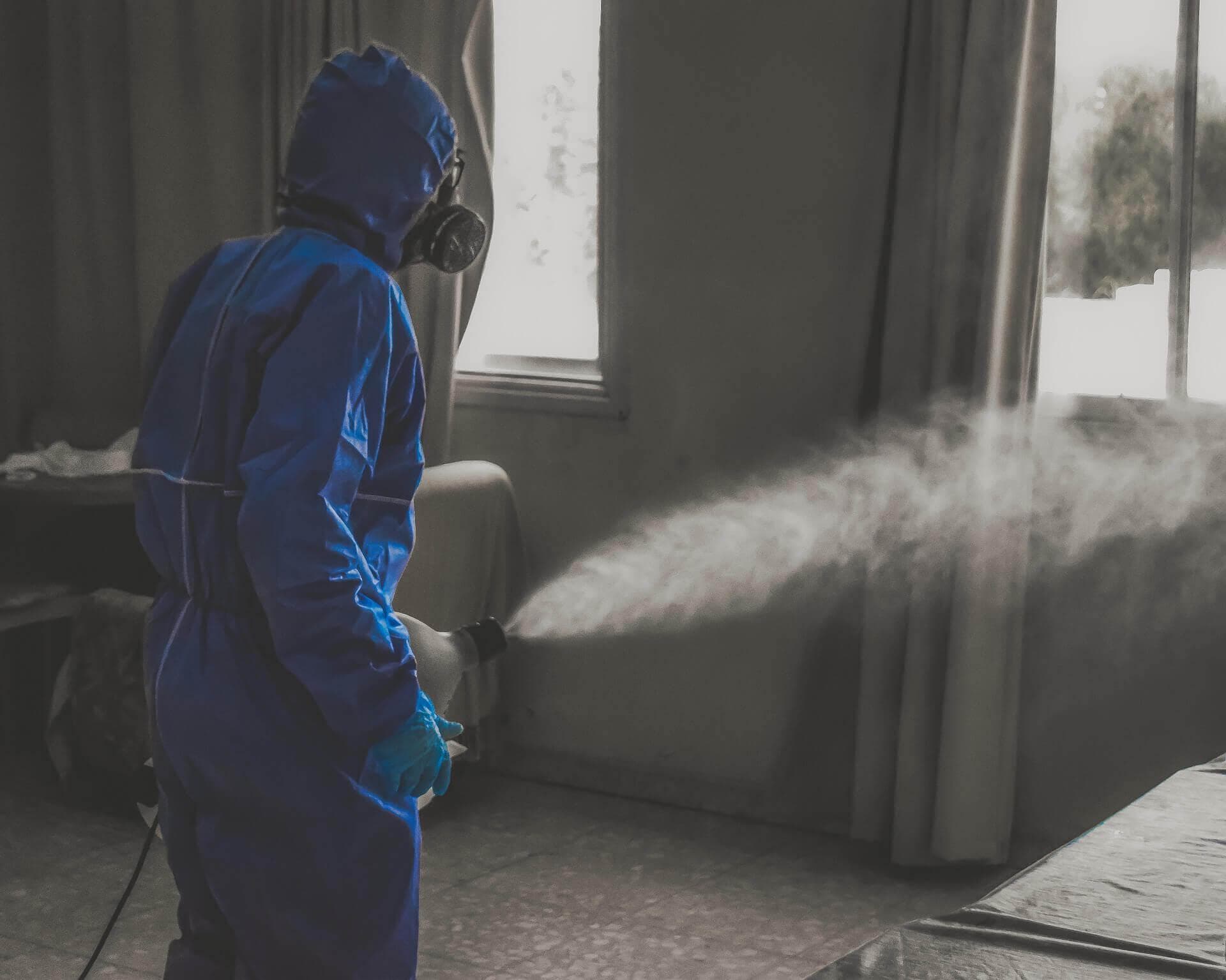 Man in a blue hazmat suit spraying disinfectant spray