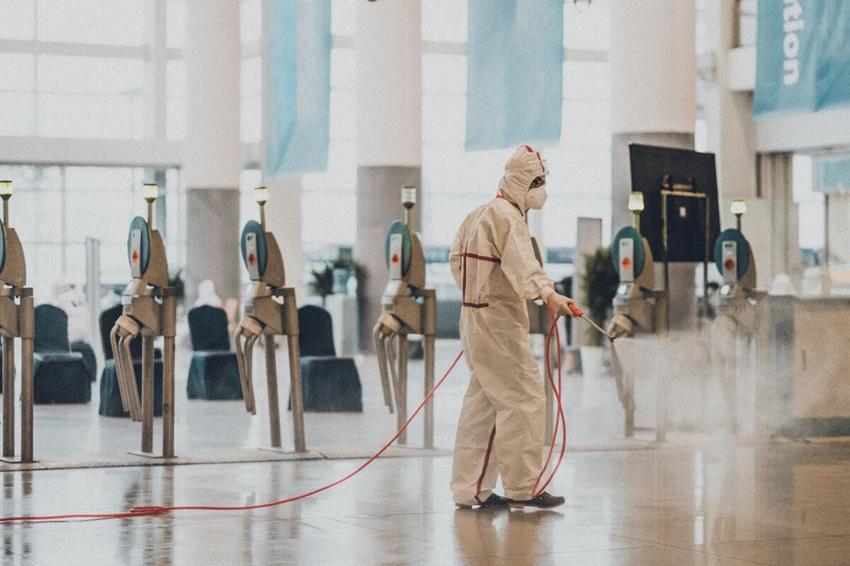 Man in a white hazmat suit spraying disinfectant spray in a mall.